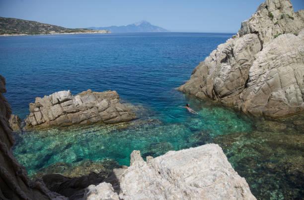 A woman is swimming in a beautiful blue lagoon, mount Athos in the background.