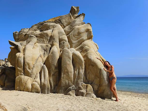 Woman posing next to large rock on sand beach