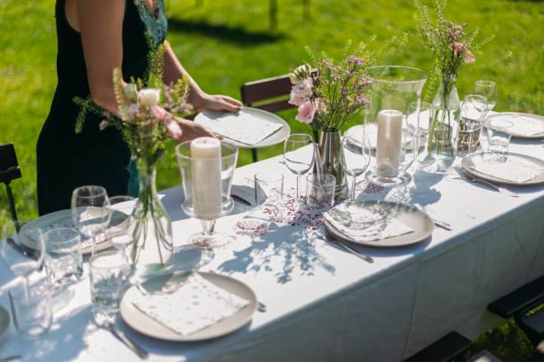 Young blonde woman setting and decorating table for lunch outdoors on a sunny day.