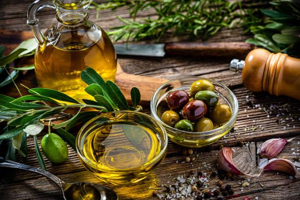 Close up view of  two glass bowls filled with olives and extra virgin olive oil shot on rustic wooden table. Olive tree branches, garlic, salt and peppercorns complete the composition. High resolution 42Mp studio digital capture taken with Sony A7rII and Sony FE 90mm f2.8 macro G OSS lens