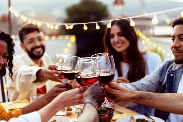 Happy people celebrating summer party toasting with red wine at home terrace.