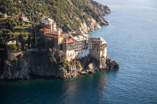 Grigoriou monastery perched on cliffs above turquoise waters, surrounded by lush coastal landscape on mount Athos, Greece