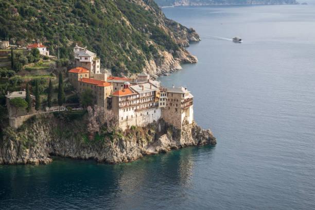 Ancient Grigorios monastery perched on coastal cliffs above turquoise waters of the Aegean sea on mount Athos