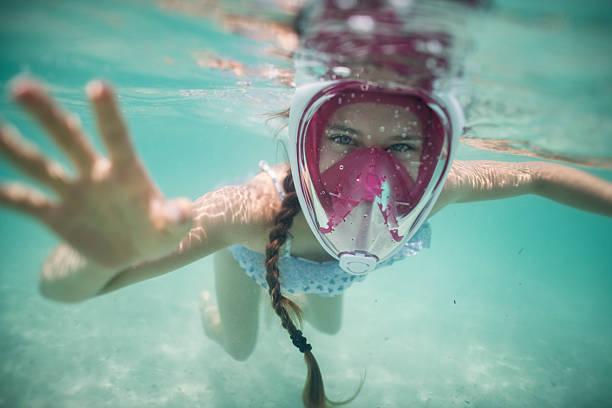 A little girl in turquoise water, wearing a full-face snorkel mask smiling at the camera. Sandy sea bed visible.
Shot with NIkon D850
